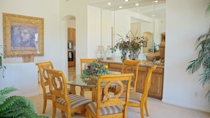 A dining area with a glass table surrounded by wooden chairs with cushioned seats. A vase with flowers is on the table, and there is a mirror on the wall. - Troon Skyline Private By Signature Vacation Rental (Scottsdale)