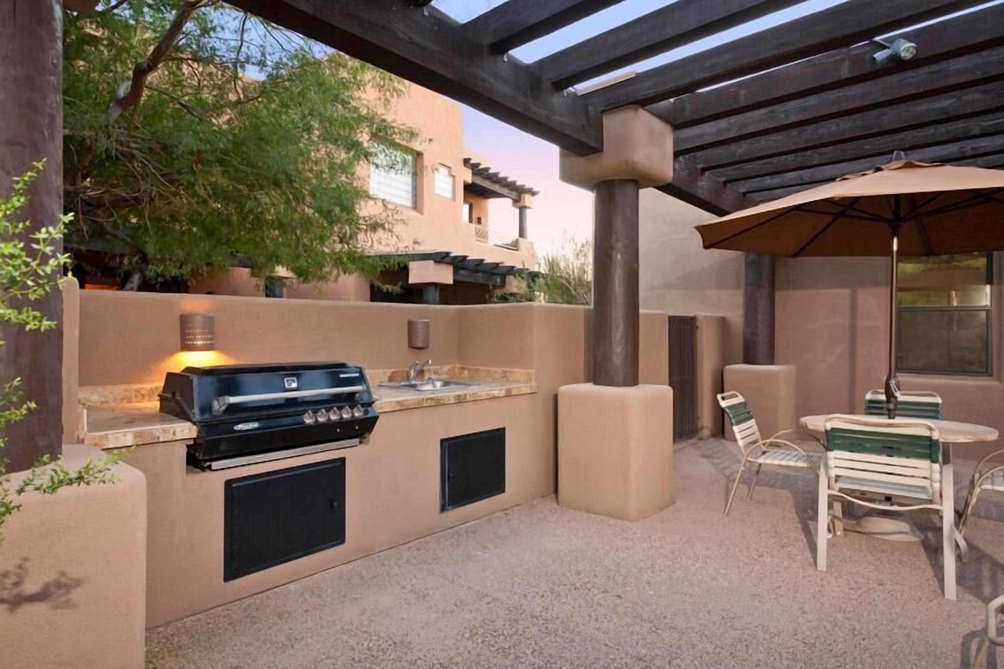 Terrassa exterior amb una barbacoa de obra, zona de seients i una pèrgola.
