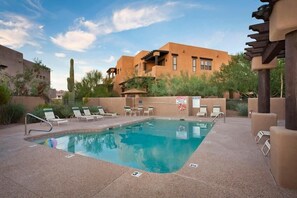 A pool area with lounge chairs, a cactus, and a building in the background. - Troon North Golf Casitas By Signature Vacation Rentals (Scottsdale)