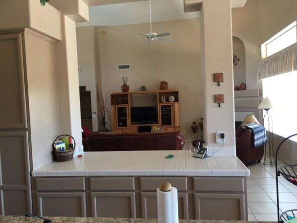 A spacious living area with a large TV, wooden cabinets, and a ceiling fan.