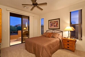 A bedroom with a bed, a ceiling fan, a nightstand with a lamp, and a painting on the wall. - Troon North Golf Casitas By Signature Vacation Rentals (Scottsdale)