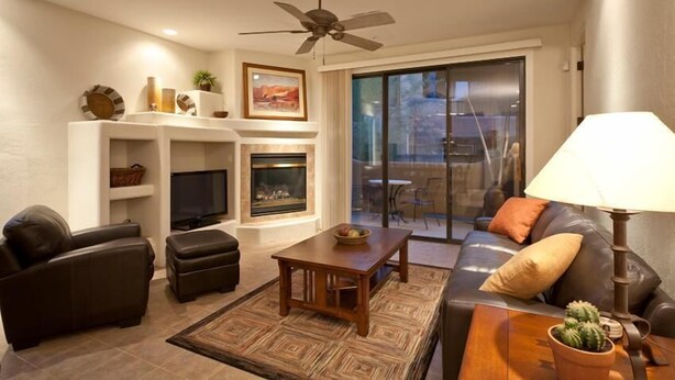 Una sala moderna con chimenea, ventilador de techo, televisor de pantalla plana y comedor con puerta de vidrio que da al exterior.