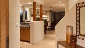 Un pasillo amplio con una cocina al fondo, una puerta de madera y una consola decorada con objetos ornamentales.