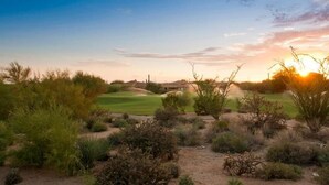 Un paysage désertique avec un terrain de golf, une végétation clairsemée et un ciel dégagé.