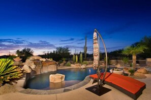 A swimming pool with a waterfall feature, surrounded by desert plants and cacti.
