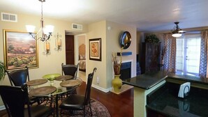 A dining area with a round table, chairs, and a chandelier. There is a fireplace with a vase of dried plants. The room has a wooden floor and beige walls. - Traditional Touch By Signature Vacation Rentals (Scottsdale)