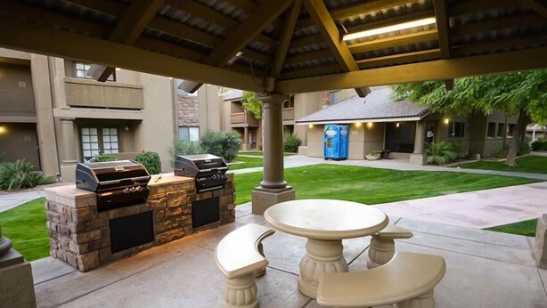 An outdoor patio with a stone barbecue and a round table with benches. - Traditional Touch By Signature Vacation Rentals (Scottsdale)