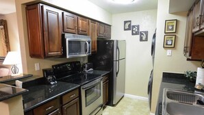 A compact kitchen with dark wooden cabinets, stainless steel appliances, and a black countertop. - Traditional Touch By Signature Vacation Rentals (Scottsdale)