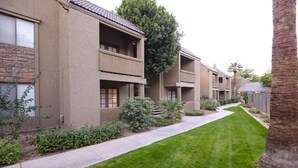 A row of modern apartment buildings with balconies, a well-maintained lawn, and a palm tree. - Traditional Touch By Signature Vacation Rentals (Scottsdale)