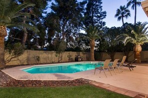A swimming pool with lounge chairs, surrounded by palm trees and a stone wall. - Thunderbird By Signature Vacation Rentals (Scottsdale)