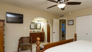 A bedroom with a bed, a ceiling fan, a television, a chair, a dresser, and a door leading to another room. - Thunderbird By Signature Vacation Rentals (Scottsdale)