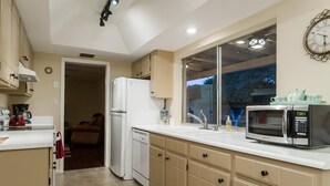 A compact kitchen with white appliances, beige cabinetry, and a large window. - Thunderbird By Signature Vacation Rentals (Scottsdale)