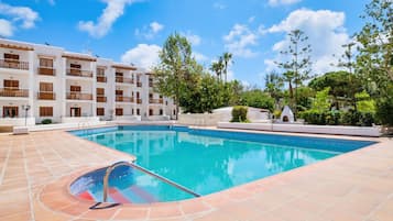 Una piscina con solárium enlosado, rodeada por un edificio de varios pisos con balcones.