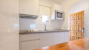Una cocina con armarios blancos, una puerta de madera, un microondas y una ventana con persiana.
