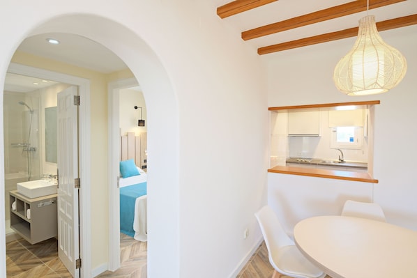 Un baño moderno con ducha, lavamanos e inodoro. Se ve una puerta blanca que da a otra habitación.