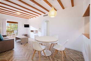 Un interior moderno con una mesa de comedor redonda, sillas blancas, un sofá y un televisor montado en la pared.