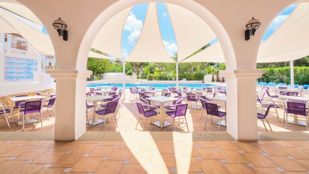 Un área de patio al aire libre con mesas y sillas, una piscina y vistas a zonas verdes.