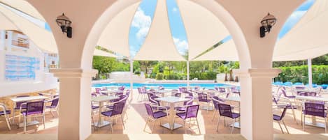 An outdoor patio with tables and chairs, a pool, and a covered area with arches.