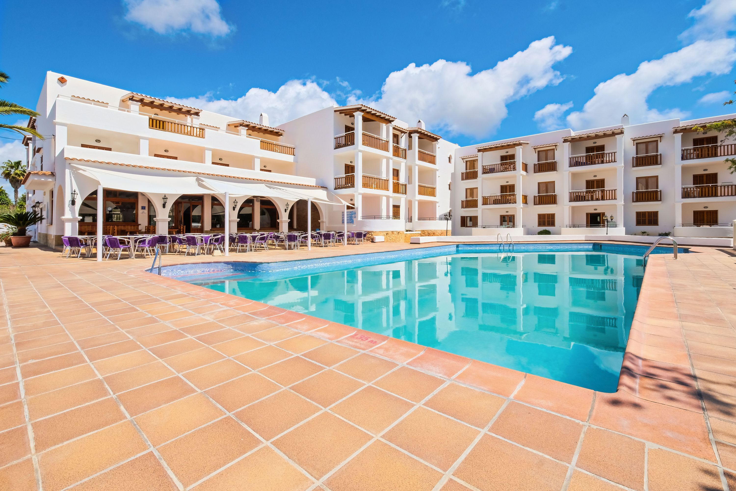 A hotel with a swimming pool, outdoor seating, and multiple balconies.