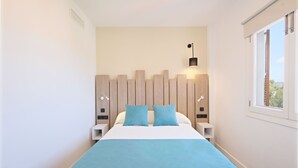 Un dormitorio moderno con una cama, dos almohadas, una mesita de noche y una lámpara de pared, además de un ventanal.