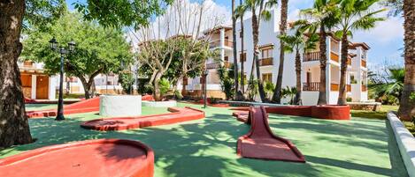 Un patio de resort con palmeras, una piscina y un edificio con balcones.