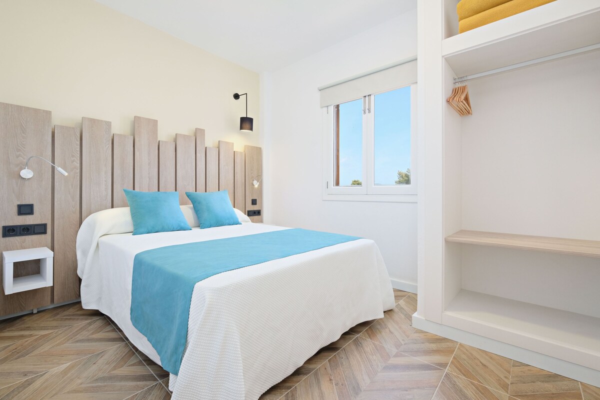 A modern bedroom with a bed, wooden headboard, bedside tables, a window, and a built-in shelf.