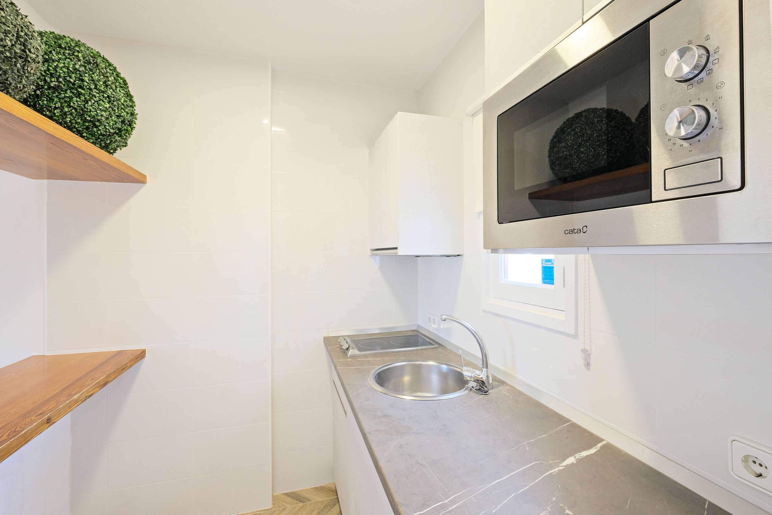 Eine moderne Küche mit Spüle aus Edelstahl, einem eingebauten Backofen und einem Holzregal.