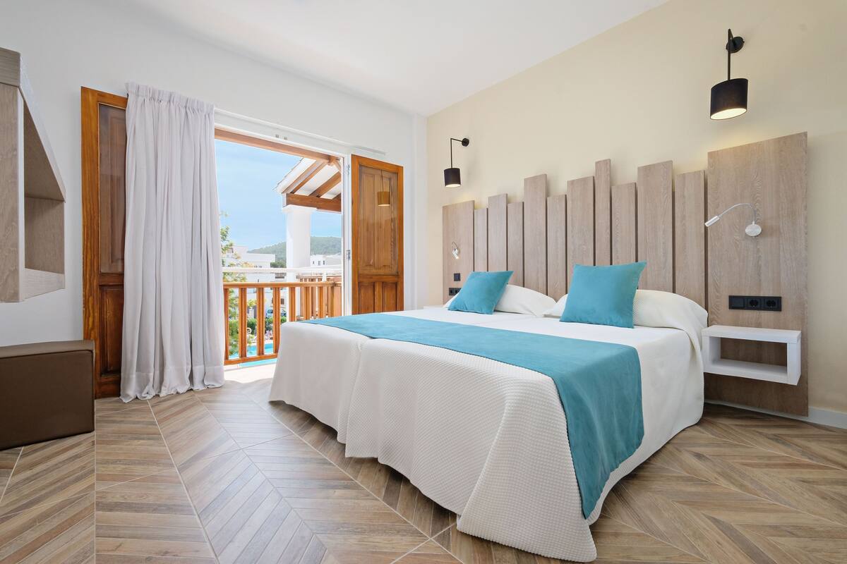 Une chambre dotée d’un grand lit, d’une tête de lit en bois, d’un balcon avec une balustrade en bois et d’une vue sur l’extérieur.