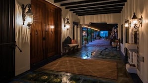 A hallway with wooden doors, wall-mounted lights, and a patterned rug.