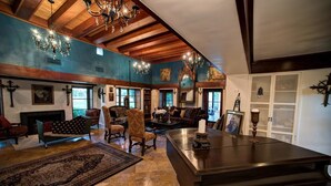 A spacious living room with a fireplace, wooden beams, and a chandelier.