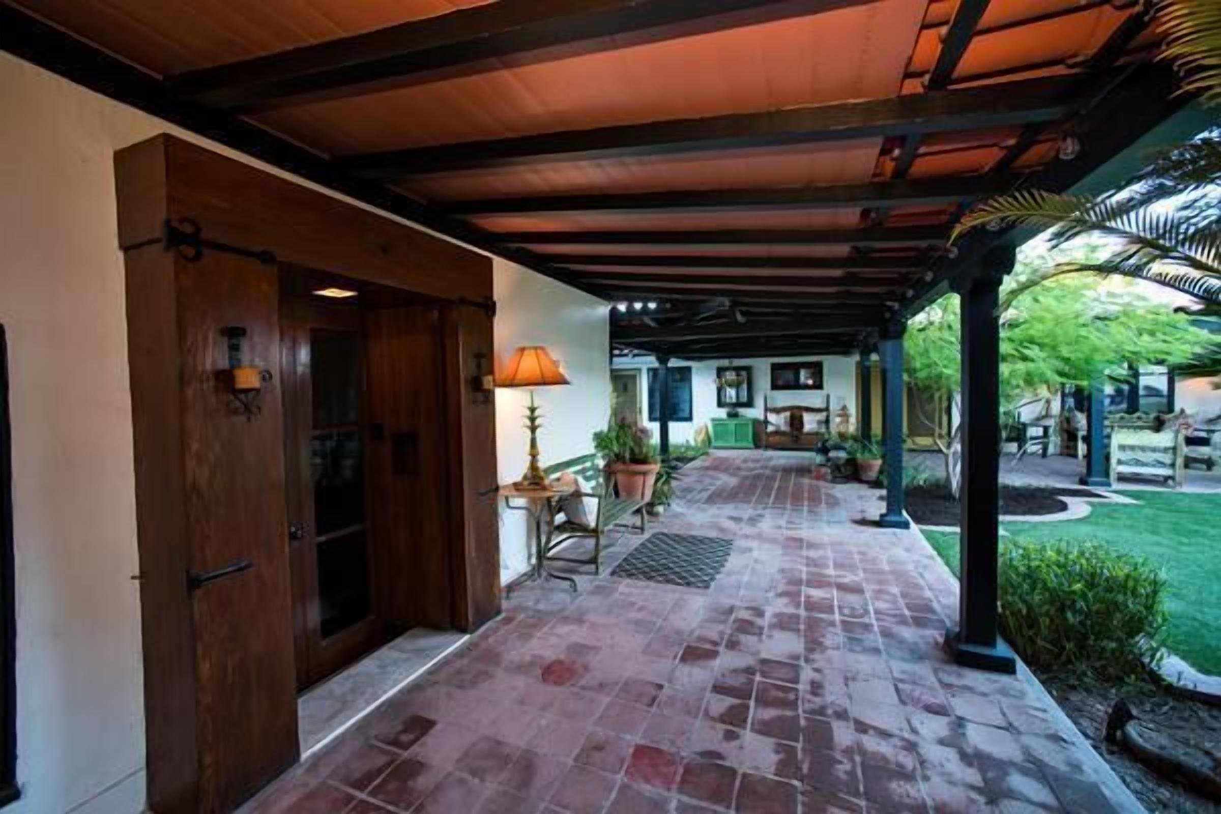 A covered outdoor area with a brick floor, wooden doors, and a lamp.