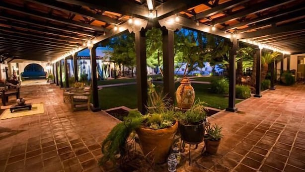 A covered outdoor area with a tiled floor, potted plants, and a view of a landscaped garden.