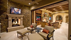 A spacious living room with a stone fireplace, comfortable seating, and a television mounted above it. - Bella Estate By Signature Vacation Rentals (Scottsdale)