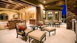 A spacious indoor area with a stone wall, a ceiling fan, and a seating area with chairs and ottomans. - Bella Estate By Signature Vacation Rentals (Scottsdale)