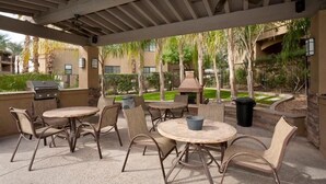 Un espace extérieur aménagé en terrasse, avec des tables et des chaises rondes, un ventilateur de plafond et un barbecue.
