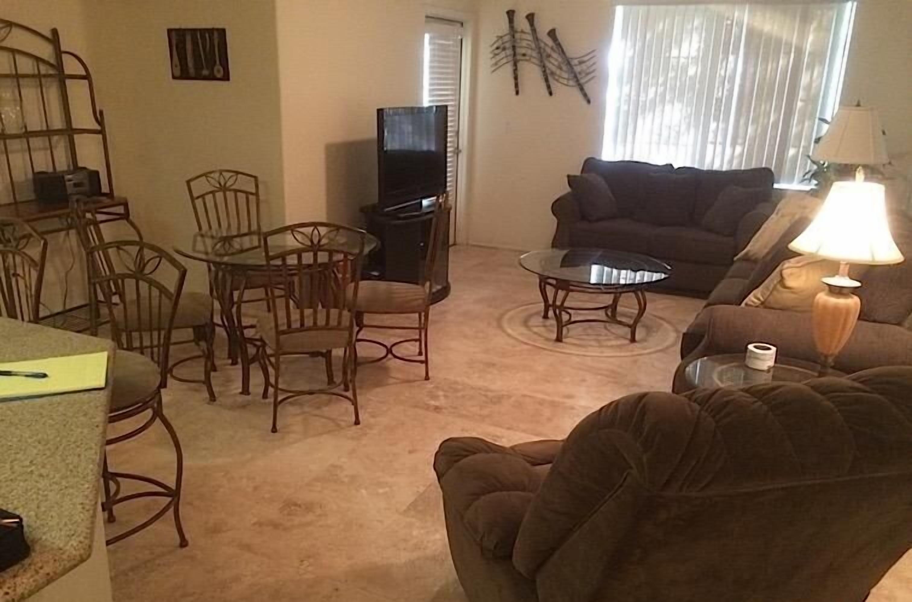 A living room with a television, a sofa, a coffee table, and a dining area with chairs.