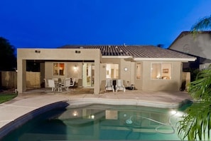 A modern house with a swimming pool, patio furniture, and a well-lit interior. - Augusta On The Green by Signature Vacation Rentals (Mesa)