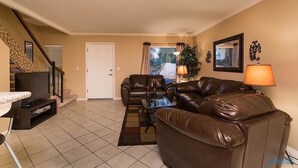 A living room with a brown leather sofa, a television on a stand, a patterned rug, and a staircase with a railing. - Arizona Grande By Signature Vacation Rentals (Phoenix)