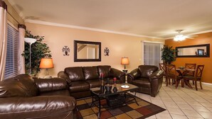 A living room with a brown leather sofa, a coffee table, and a dining area with a table and chairs. - Arizona Grande By Signature Vacation Rentals (Phoenix)