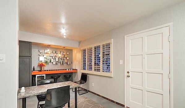 A compact kitchen with a dining area, featuring a marble countertop, black chairs, and a wall-mounted light fixture. - Amour By Signature Vacation Rentals (Scottsdale)