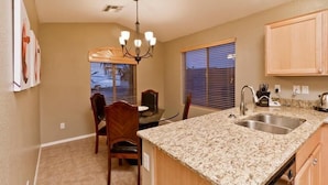 A kitchen with granite countertops, wooden cabinets, a chandelier, and a dining area with a table and chairs. - All Star By Signature Vacation Rentals (Chandler)