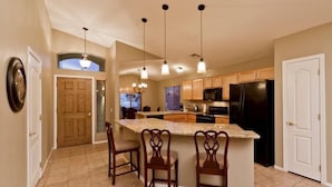 A kitchen with a central island, pendant lights, wooden cabinets, and a refrigerator. - All Star By Signature Vacation Rentals (Chandler)