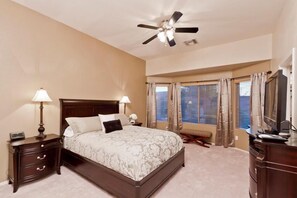 A bedroom with a bed, two bedside tables, a ceiling fan, a window with curtains, and a dresser.