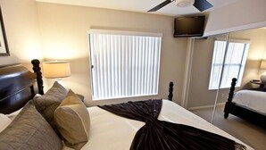 A hotel room with a bed, a television, a window with blinds, and a ceiling fan. - Admirals House By Signature Vacation Rentals (Scottsdale)