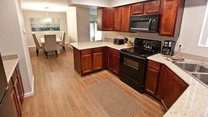 A compact kitchen with wooden cabinets, a microwave, stove, and a dining area with chairs. - Admirals House By Signature Vacation Rentals (Scottsdale)