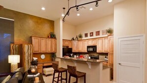 A modern kitchen with wooden cabinets, a central island with bar stools, and a microwave. - Acacia Loft By Signature Vacation Rentals (Cave Creek)