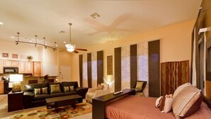 A modern bedroom with a bed, a desk, a sofa, and a chair. There is a kitchen area visible in the background. - Acacia Loft By Signature Vacation Rentals (Cave Creek)