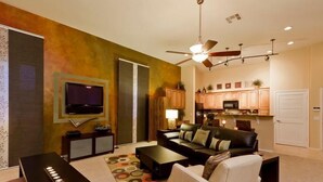 A modern living room with a flat-screen TV, a ceiling fan, and a kitchen area with wooden cabinets. - Acacia Loft By Signature Vacation Rentals (Cave Creek)