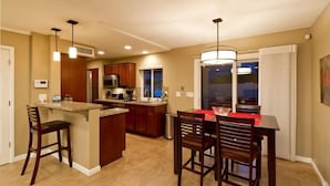 A modern kitchen with a central island, bar stools, and a dining table with chairs. - 19th Hole By Signature Vacation Rentals (Phoenix)