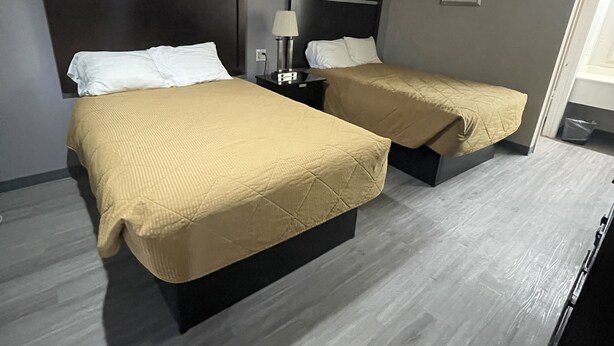 A hotel room with two beds, each with a headboard and a bedside table with a lamp. - Kinder Inn (Kinder)